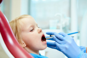 Pediatric dentist examining little girls teeth in the dentists chair